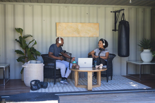 Diverse podcast co-hosts recording conversation in shipping container studio with laptop and mics