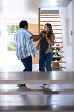 Diverse couple laughing and holding forearms in modern entry near floating staircase and bench