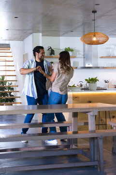 Couple dancing and holding hands near kitchen island with warm lighting and wooden bench foreground