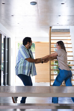 Couple laughing and standing in home entryway near wooden stairs and glass doors, watch visible