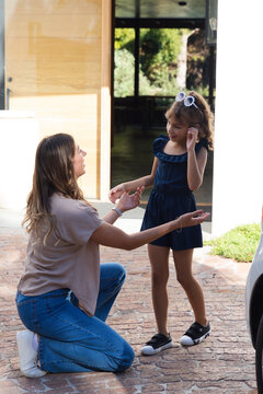 Woman kneeling, reaching, girl standing wearing heart headband at home entrance on brick driveway