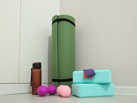 Green Rolled Yoga Mat Stands Beside Water Bottle, Foam Blocks, And Textured Massage Balls On Clean Indoor Floor, Calm Minimal Wellness Setup For Stretching, Balance, Recovery, And Home Training
