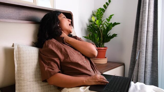 Tired woman stretching neck while sitting at home, fatigue, body pain, stress, sedentary lifestyle, digital burnout and physical discomfort concept