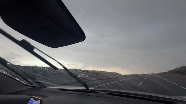 Driver travels through heavy rain in front interior view as windshield wipers clear the road ahead, showing adverse weather driving, navigation use, road safety, and vehicle travel during storm