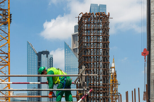 Construction worker in safety harness and hard hat working on scaffolding with Dubai skyscrapers in the background on sunny day