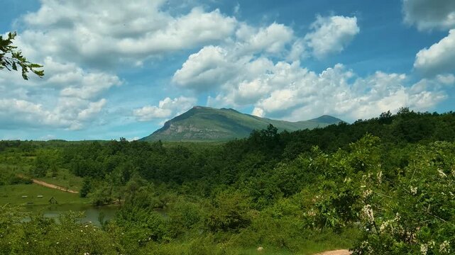 Lush green hills roll beneath a bright blue sky. Vrmdza Lake, Serbia