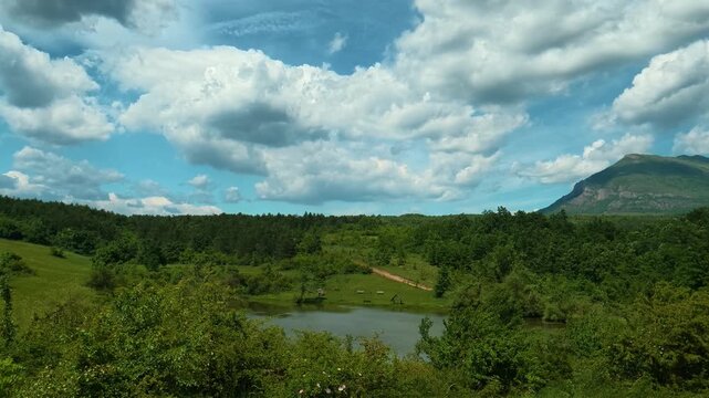 Vast green hills roll beneath a bright blue sky. Vrmdza Lake, Serbia