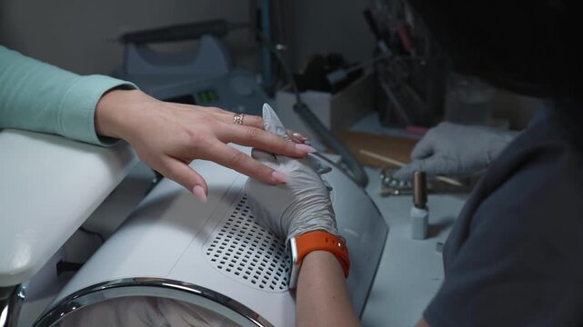 Nail technician moves glitter particles with magnet through freshly applied gel, creating abstract pattern on nail in beauty salon