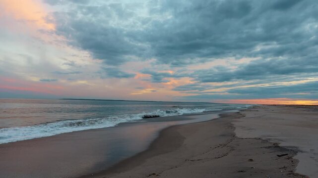 Sunset at the beach with waves and clouds in the sky. Waves roll onto the sand as clouds cover the sky during sunset near the water.