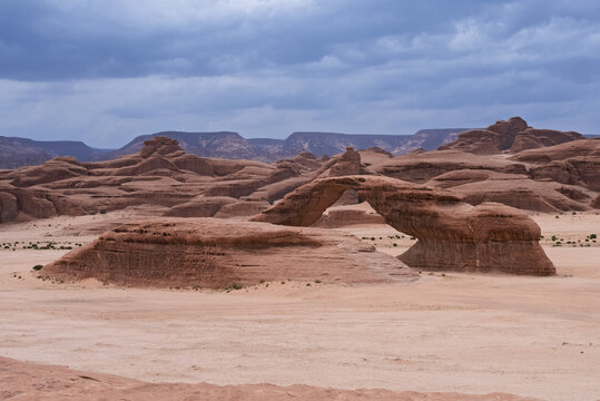 Wide Angle Eye Level Landscape View of Rainbow Rock Natural Sandstone Arch Formation in Desert Plateau Under Overcast Sky, AlUla, Saudi Arabia