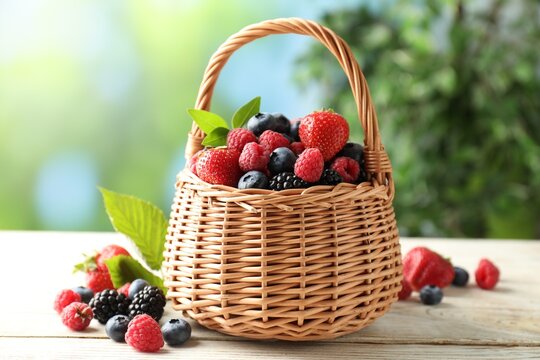 Many different berries in wicker basket on white wooden table, closeup