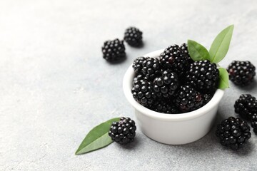 Ripe blackberries with leaves in bowl on light grey table, closeup. Space for text © New Africa