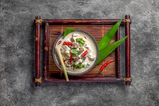 Thai chicken mushroom coconut milk soup tom kha gai in gray bowl with thai spices. Top view