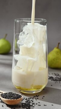 Oat milk pours over ice and pear syrup in glass, creating base for black sesame pear latte during autumn drink preparation.