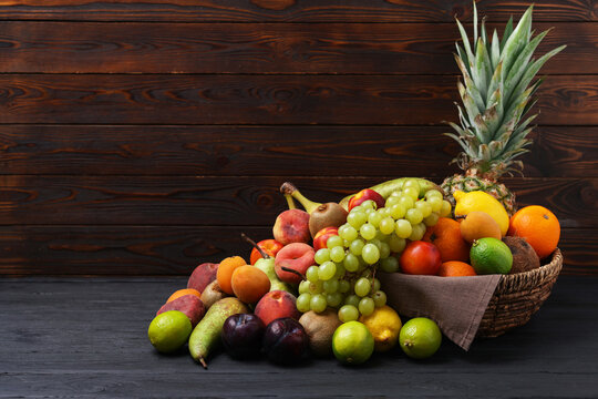 Different fresh fruits in wicker basket on black wooden table, space for text