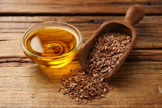 Flax seeds in scoop and bowl of oil on wooden table, closeup