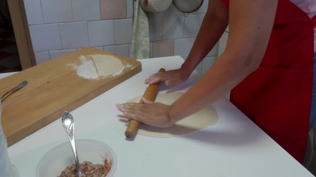 A focused cook smoothly rolls fresh dough with a wooden rolling pin. They work passionately at a clean white table in a bright kitchen during a joyful meal preparation routine.