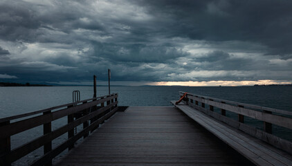 Obraz premium Wooden pier extends into calm waters under brooding sky