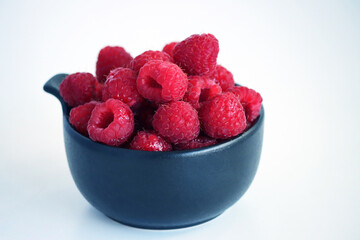 Raspberries in a black cup against a light background. Close-up of juicy, ripe berries. Food. Sweet berries harvested by farmers during the summer season. Organic. Vitamins. healthy raspberries. © Tatuss