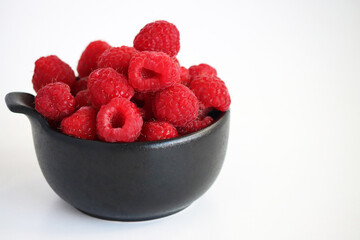 Raspberries in a black cup against a light background. Close-up of juicy, ripe berries. Food. Sweet berries harvested by farmers during the summer season. Organic. Vitamins. healthy raspberries. © Tatuss