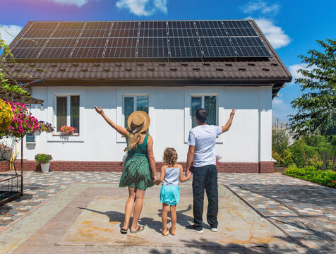 A family looks at solar panels on the roof of a house. Selective focus.