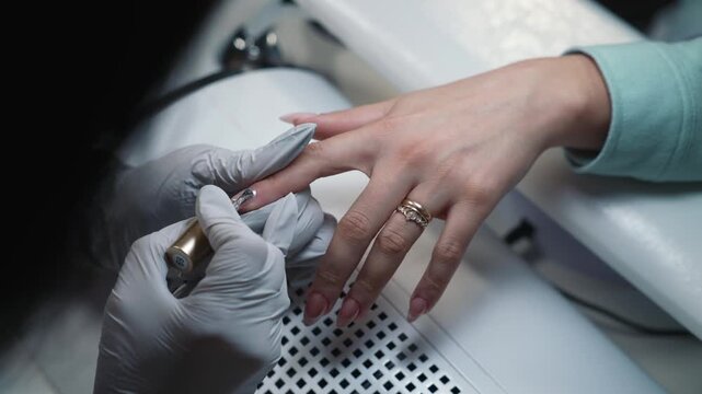 Creating magnetic glitter pattern on gel nail coating using magnet during professional manicure procedure in beauty salon