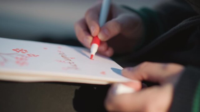Close up of person hands drawing with red marker on white paper creating cherry blossom design. Soft natural light highlights focused hand movements and smooth texture of notebook page