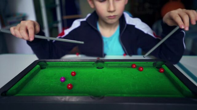 A seven-year-old boy spends his free time playing table billiards alone in his bedroom, illustrating childhood boredom, staying home, indoor leisure, quiet recreation, and ways to entertain himself