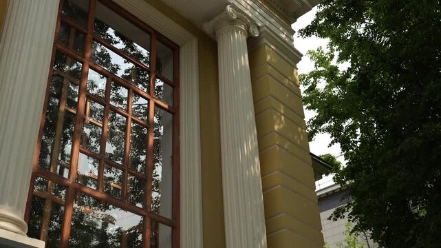 Classical facade with fluted Ionic column and multi-pane wooden window under dappled sunlight reflecting tree canopy, with architecture, column, ionic, fluting detail