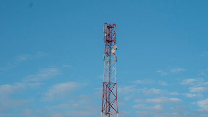 A tall communication tower rises majestically against the backdrop of a pristine blue sky, adorned with a few wispy clouds drifting by. This impressive structure is situated in a tranquil rural area,  © Сергей Семенов