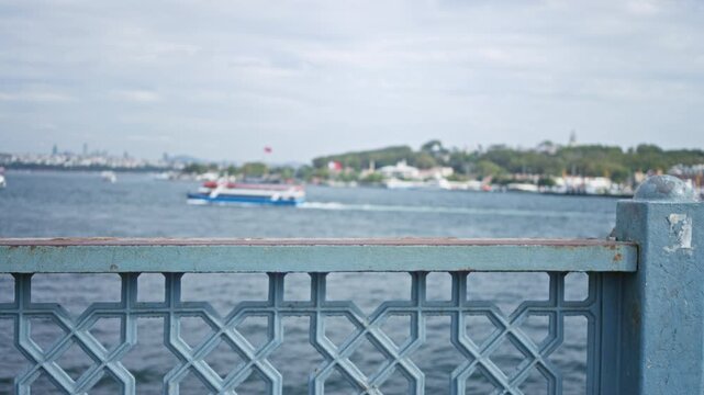 Blue metal railing in sharp foreground with defocused bosphorus sea and ferry, bokeh city skyline background outdoor; background backplate copyspace calm.