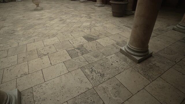 Worn stone tile courtyard with classical columns viewed from low oblique angle showing diagonal paving pattern and textured surface, with stone, tile, floor, column detail