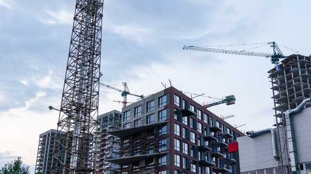 Modern high-rise buildings under construction with cranes against a cloudy sky
