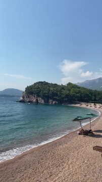 Scenic vertical shot of quiet sand and pebble beach with clear turquoise water gently lapping the shore. Sveti Stefan, Montenegro