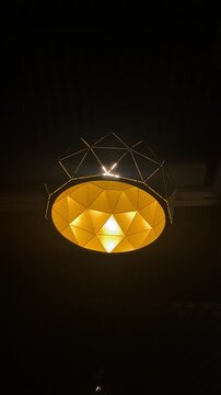 Swinging modern geometric pendant lamp glows with warm golden light in dark space