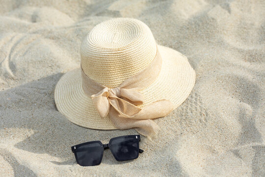 Straw sun hat with ribbon and black sunglasses resting on sandy beach, ideal for summer vacation and outdoor activities. Summer outfit and vacation concept. Copy space. Top view