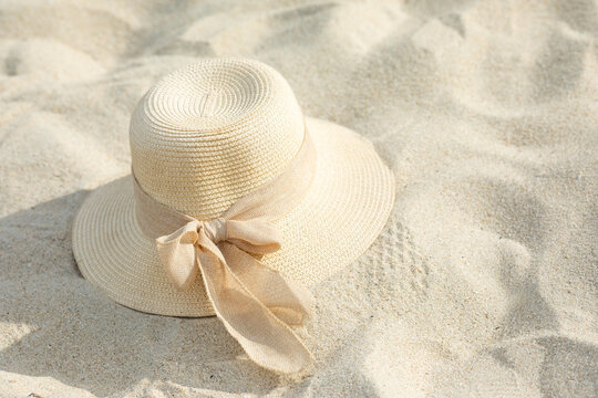 Wide-brimmed straw hat with a ribbon lying on fine sand at a beach, showcasing a summer accessory for sun protection and style. Beach fashion concept. Copy space