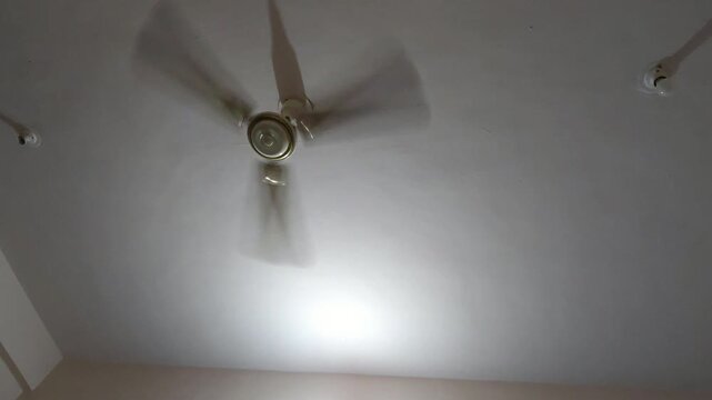 A slow-moving fan casts rhythmic shadows across an empty office space, highlighting the continuous energy consumption required to manage rising temperatures in urban concrete jungles.