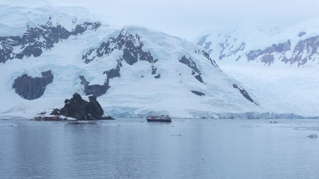 December 30, 2025 - Paradise Bay, Antarctica: A Cruise Ship Sails Near Brown Station Research Science Base. Red Buildings. Snow Covered Mountains