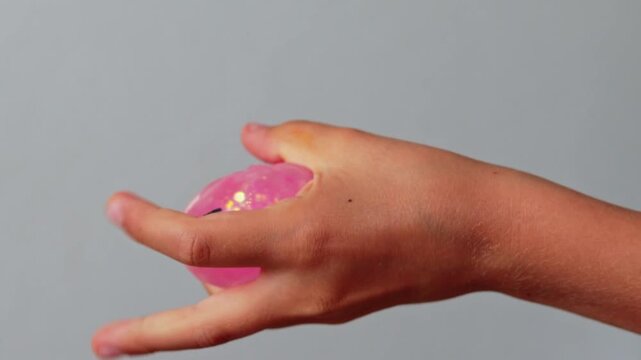 Child's hand squeezes a pink squishy dumpling toy, showcasing the deformation and return to shape in a playful indoor setting against a neutral background