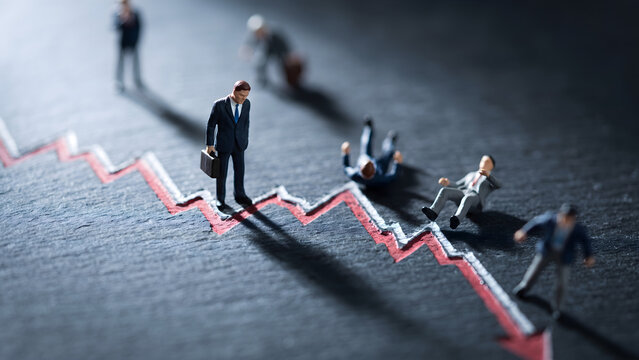 Miniature businessmen on declining red graph line symbolizing financial crisis and economic crash