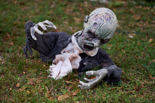 Creepy zombie decoration crawls from the ground on a grassy lawn. Tattered clothes, decayed face, and reaching hands create a scary Halloween yard scene.