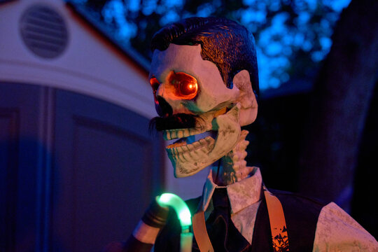 Side view of a skeleton bartender pouring a drink with a neon tube. Red glowing eyes and formal clothes create a spooky Halloween yard prop.