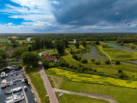 High angle wide horizontal aerial drone photograph of De Koe windmill, historic earthwork ramparts, marina boats, and dramatic storm sky in Veere, Zeeland, Netherlands on sunny summer day