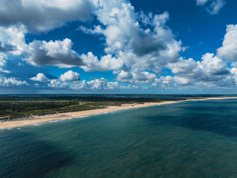 High angle wide horizontal aerial drone photograph of North Sea beach coastline, sand dunes, sea water, and cloudy blue sky at Neeltje Jans, Zeeland, Netherlands on sunny summer day