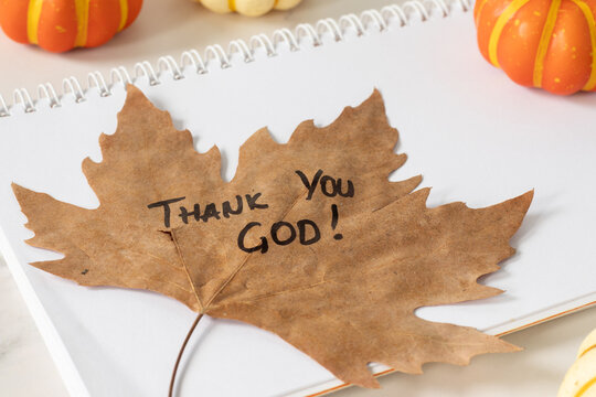 Thank You God, handwritten quote on an autumn leaf with pumpkin decoration. Christian thanksgiving and gratitude concept.