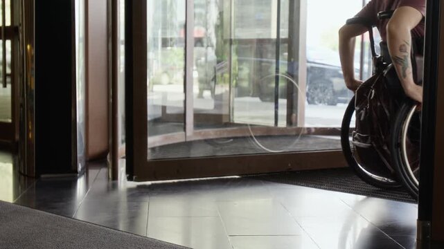 Girl with disability wheeling herself through revolving door of modern hotel. Video is ideal for promoting accessibility, social inclusion, and diversity in workplace