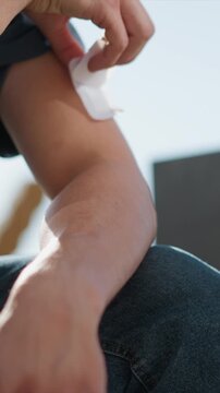 Close up of person applying adhesive bandages to their arm and hand revealing red marks on skin. process involves careful placement with one visible white pad against bare flesh emphasizing