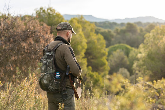 Hunter standing checking terrain with rifle in forest