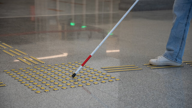 A blind woman walks on tactile paving. Close-up of her feet and a walking stick.